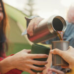 Closeup group of happy Asian friends drinking a cup of hot coffee for breakfast in vacation with camping caravan at morning. Lifestyle travel nature.